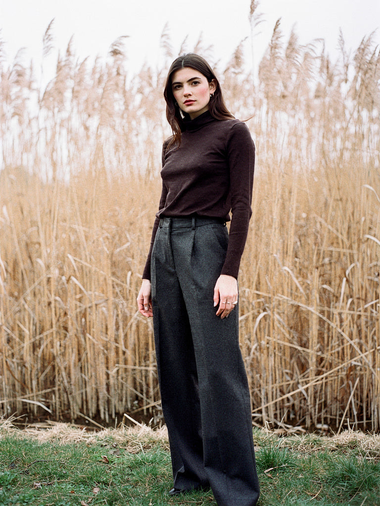 Womens wool roll neck top in treacle brown, worn with charcoal wool trousers by a bank of winter reeds