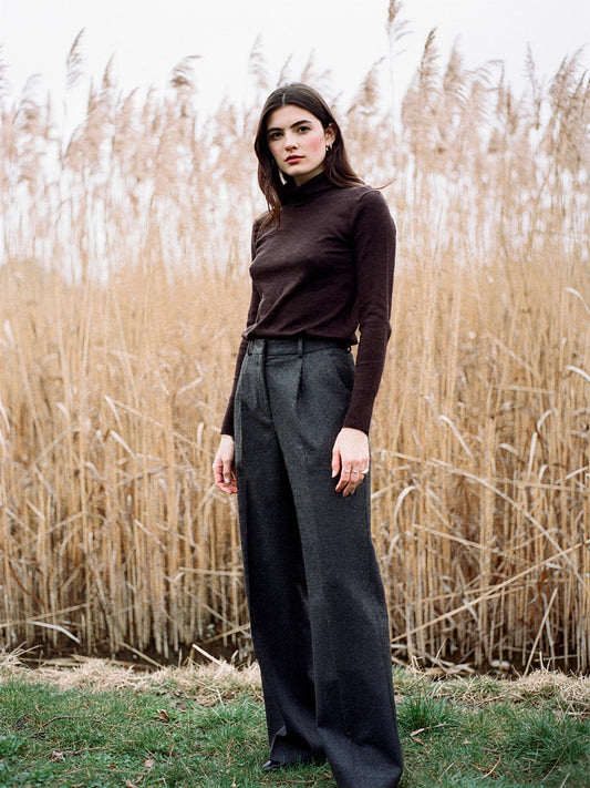 Womens wool roll neck top in treacle brown, worn with charcoal wool trousers by a bank of winter reeds