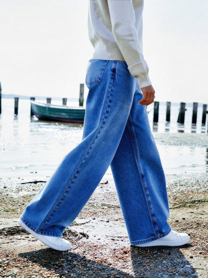 Mid Blue wide-leg jeans worn in profile on an English estuary shore