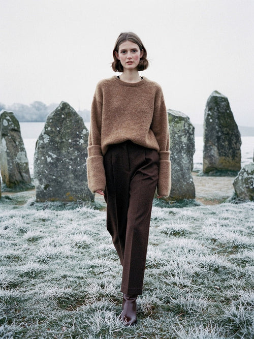 Cappuccino alpaca jumper worn with dark brown trousers among standing stones on frosted downland