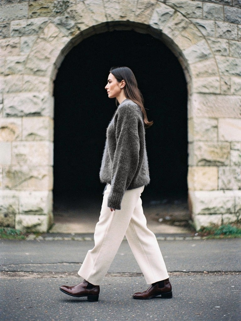 Granite grey alpaca jumper worn with cream trousers in front of a pale stone arch
