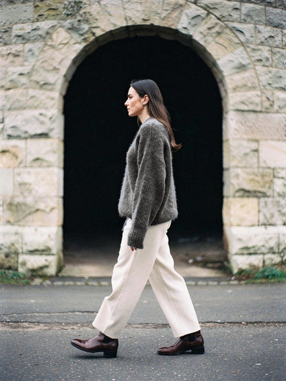 Granite grey alpaca jumper worn with cream trousers in front of a pale stone arch