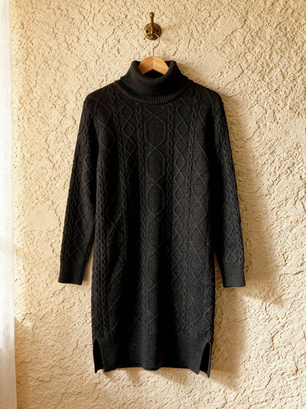 Black Aran cable-knit polo-neck jumper dress on a wooden hanger