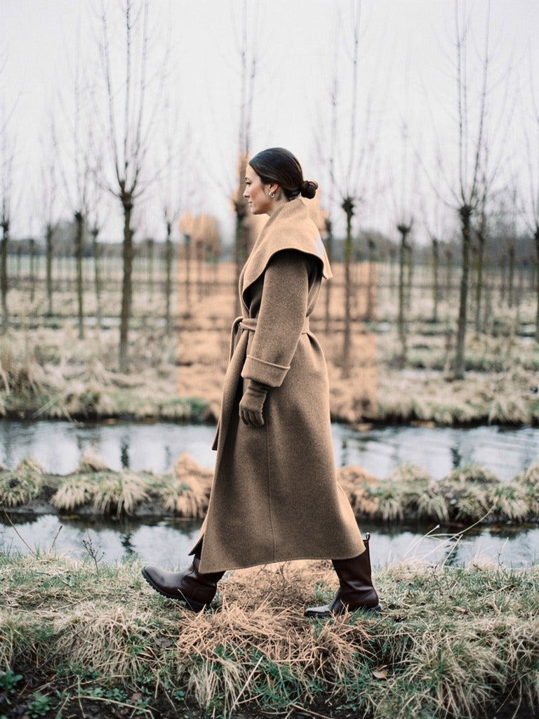 Belted wrap coat in Hickory taupe seen in profile in a winter osier bed, showing the longline cut and the plain back of the coat