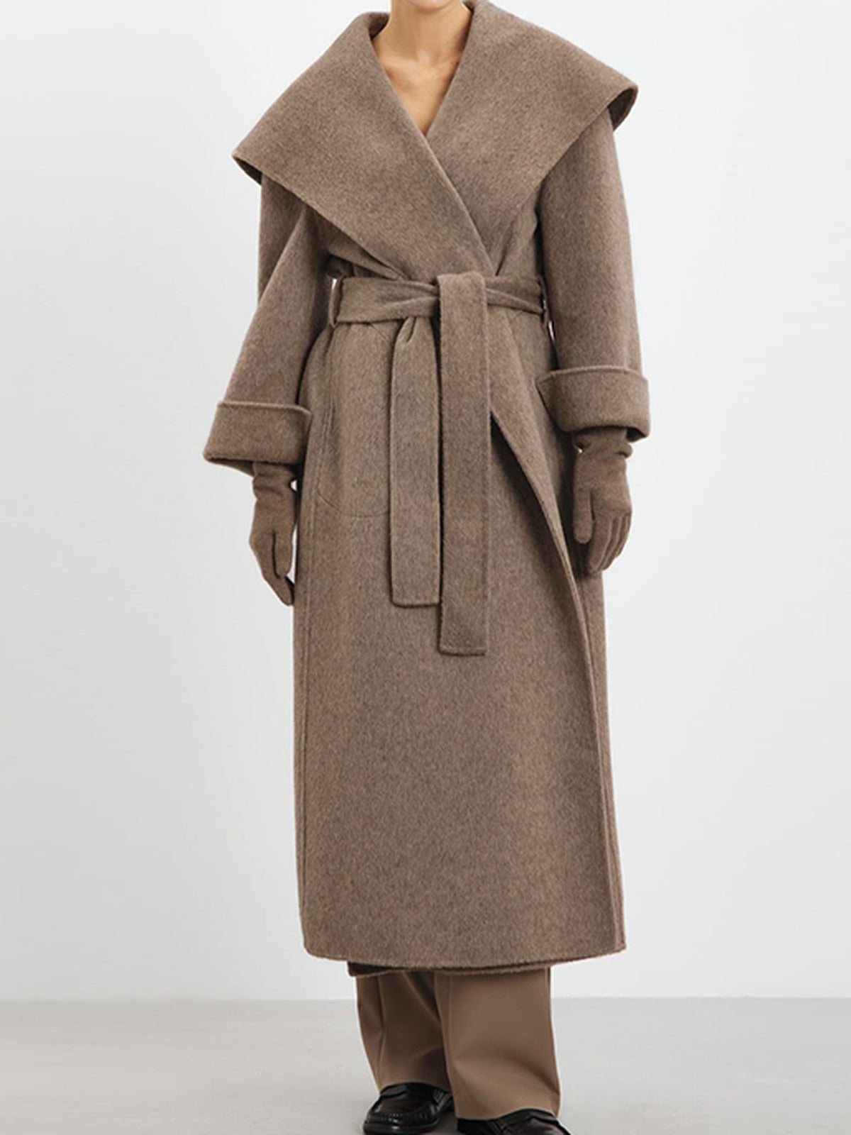 Full length view of the belted wrap coat in Hickory taupe, worn belted with the shawl collar folded back and the patch pockets at the hip