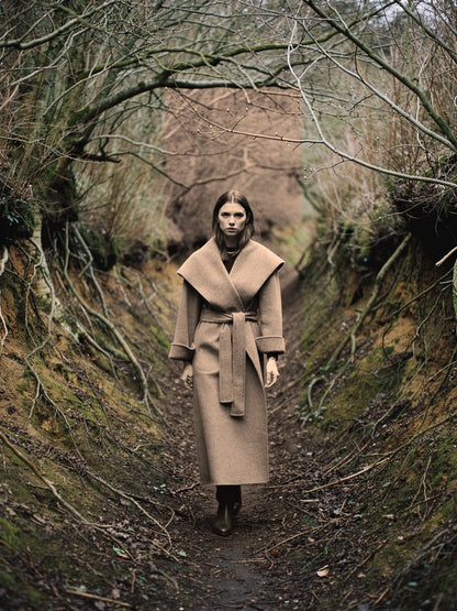 Belted wrap coat in Hickory taupe worn in a sunken English lane, deep shawl collar folded wide across the shoulders and self tie belt knotted at the waist