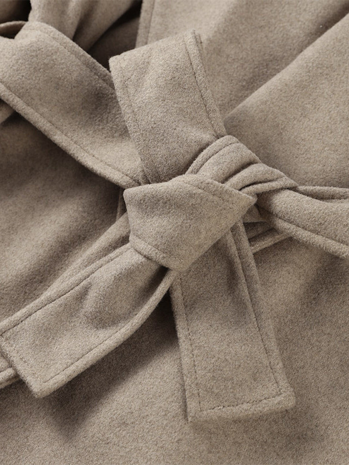 Detail of the self tie belt of the belted wrap coat, knotted flat at the waist over the brushed cloth