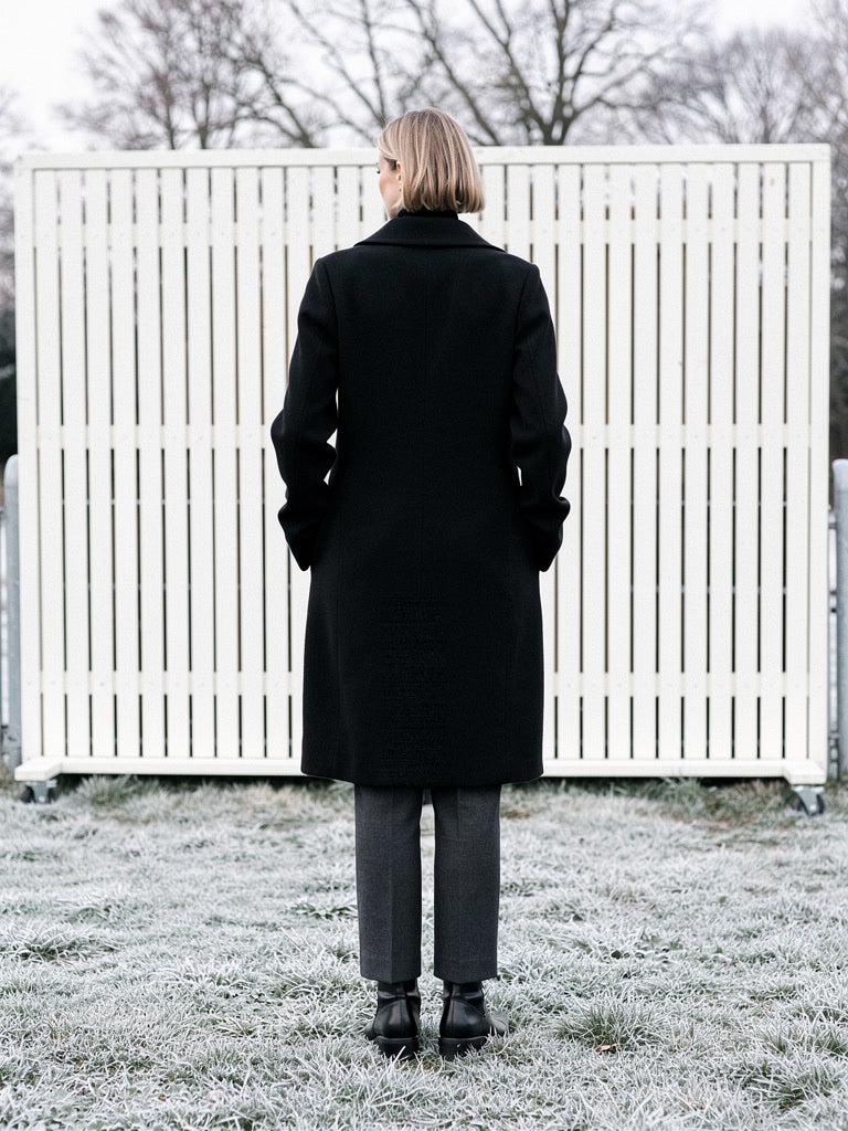 Black coat seen from the back, showing the plain longline panel and straight hem