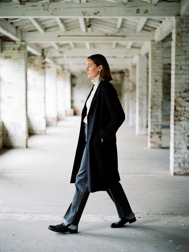 Black coat worn open and seen from the side, showing the longline cut below the knee