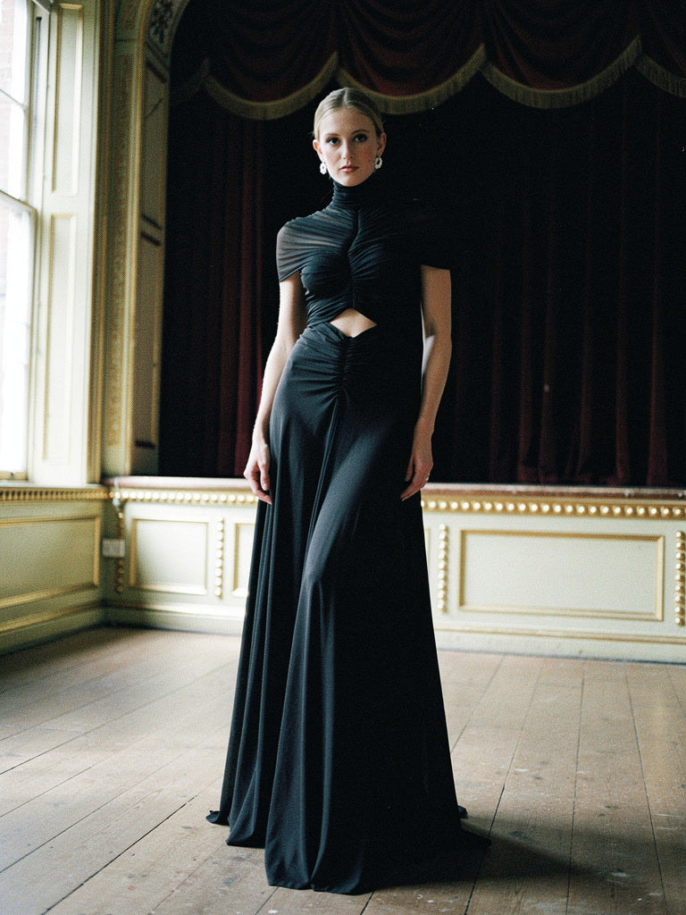 Black maxi dress with a ruched mesh bodice and cut-out waist, worn in an English country house theatre