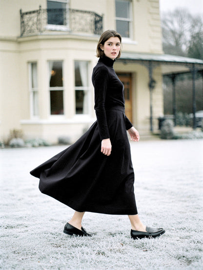 Black midi skirt with deep box pleats, worn walking in ebony with a black roll-neck jumper