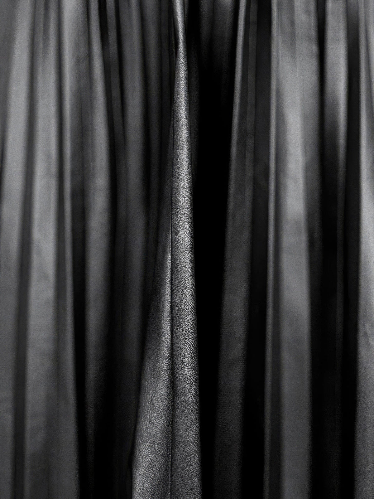 Close up of the faux leather cloth of the black pleated skirt, showing the satin sheen along each pressed knife pleat