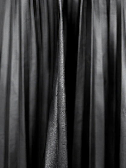 Close up of the faux leather cloth of the black pleated skirt, showing the satin sheen along each pressed knife pleat