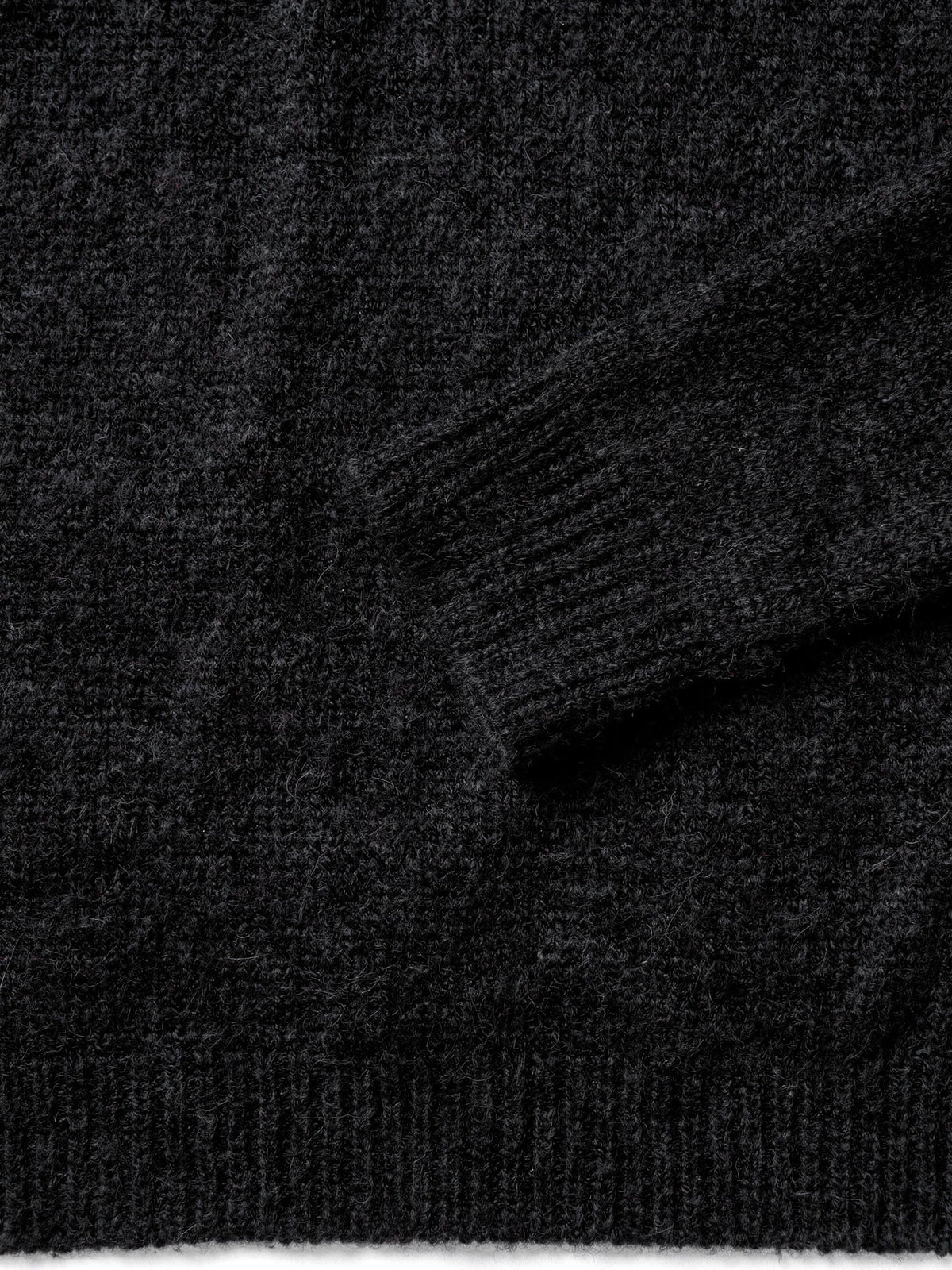 Close-up of the fine-gauge black knit, ribbed cuff and hem of the roll neck jumper
