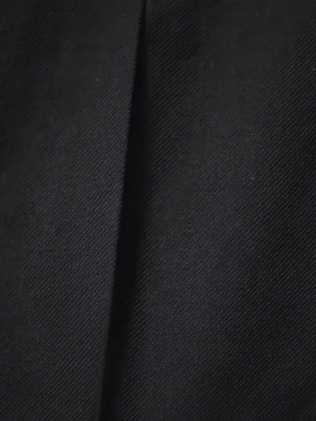 Close-up of the smooth matte twill and pressed crease of the black trousers