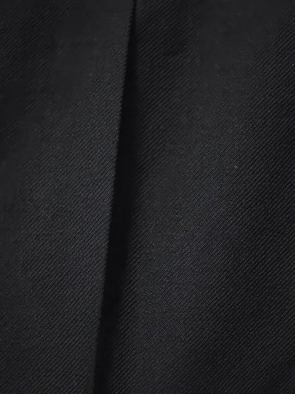 Close-up of the smooth matte twill and pressed crease of the black trousers