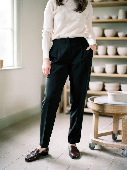 Womens black trousers with a high-rise cigarette leg, worn with a cream knit in a pottery studio