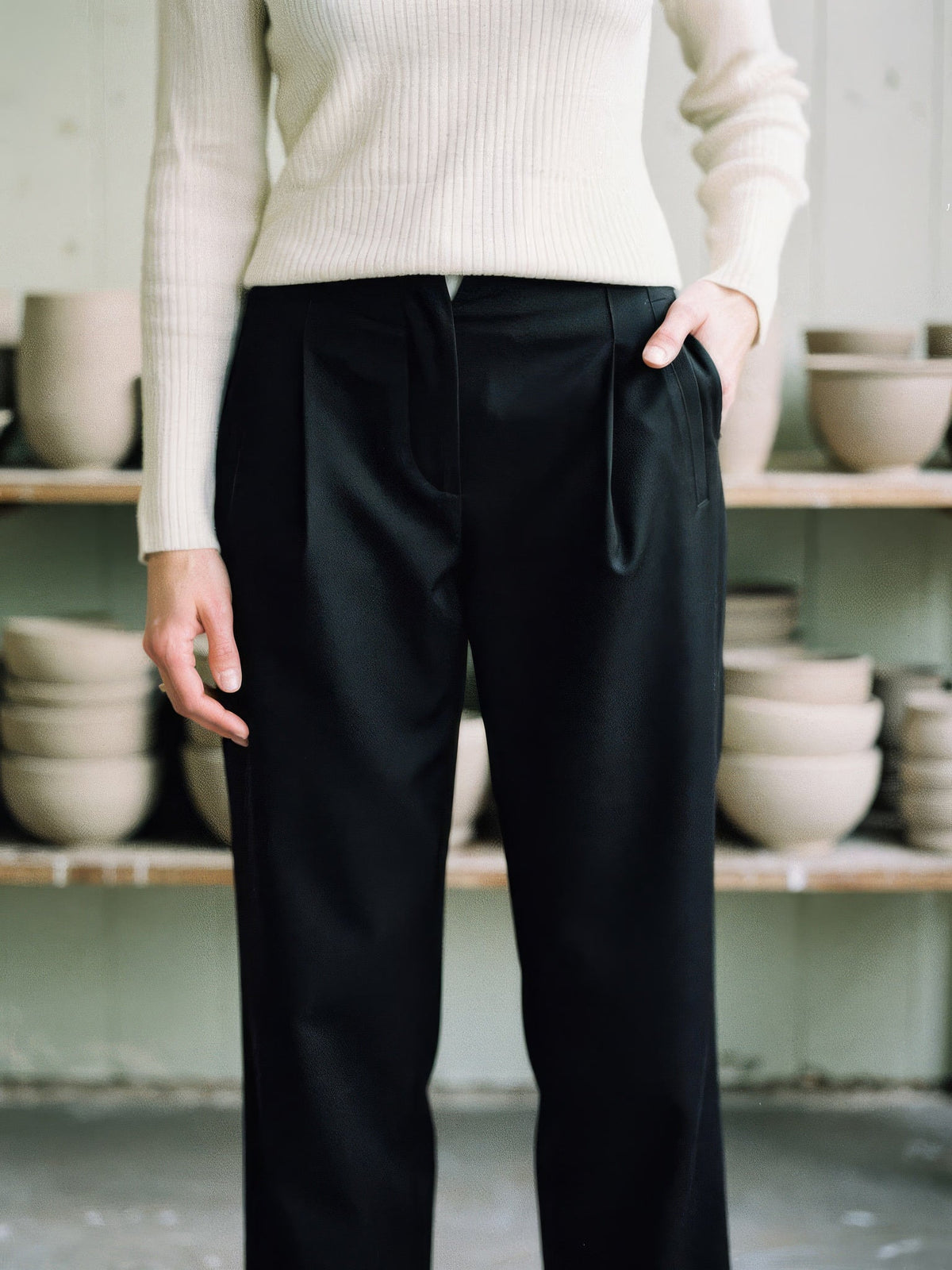 High-rise waistband, V notch and front pleats of the black trousers, worn