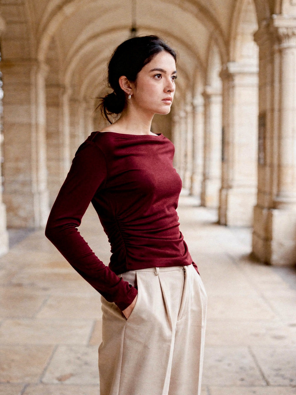 Burgundy boat neck top seen from the side in a cathedral cloister, showing the ruched side seam