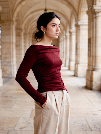 Burgundy boat neck top seen from the side in a cathedral cloister, showing the ruched side seam