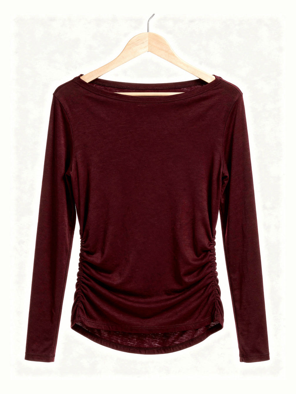 Burgundy boat neck top on a hanger showing the wide slash neckline and the ruched side seams