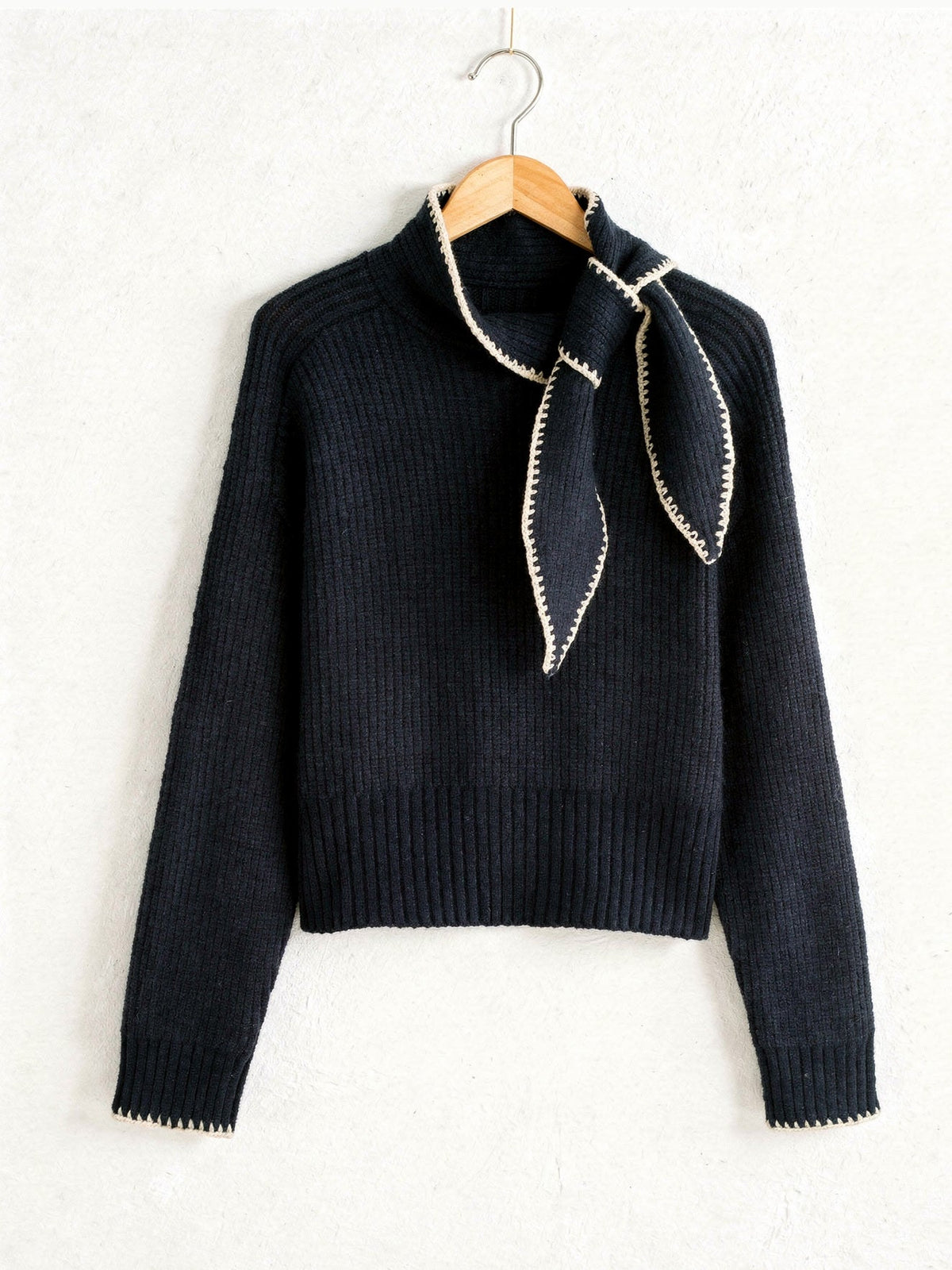 Bow neck jumper in Fathom Navy with cream contrast whipstitch, on a wooden hanger