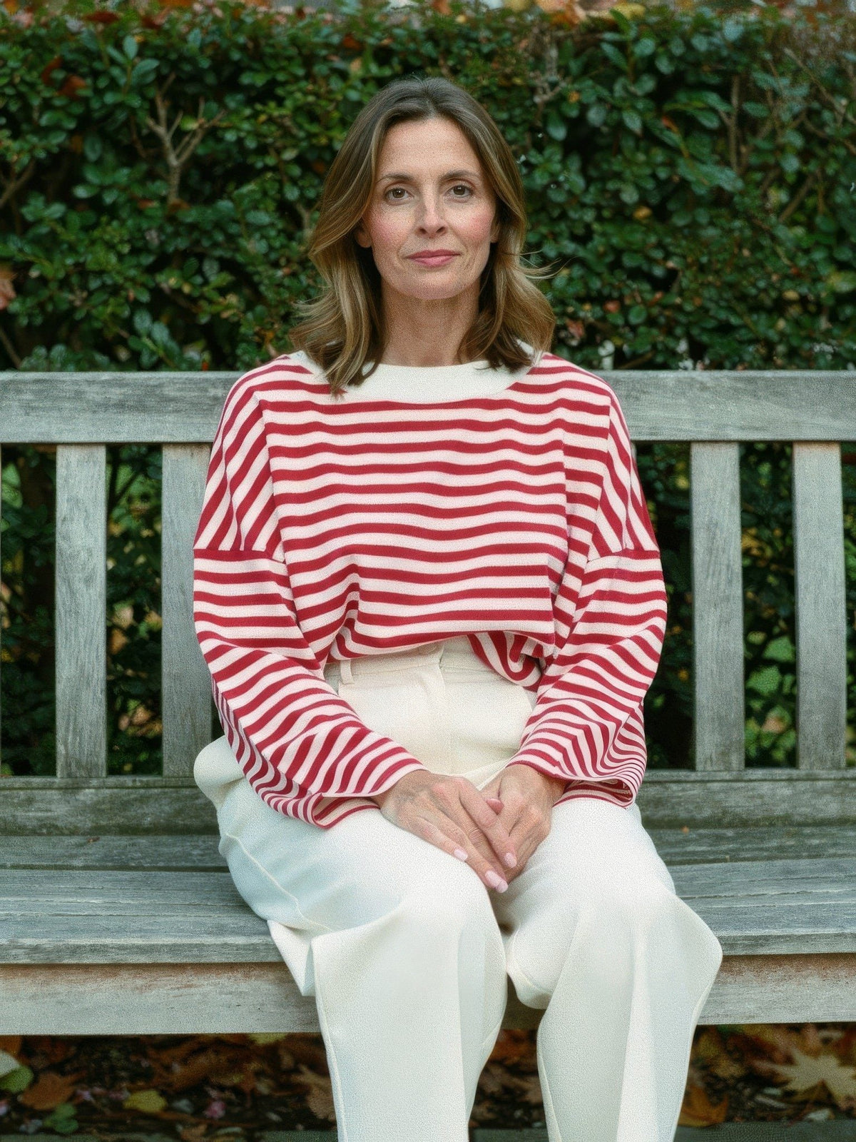 Woman wearing the cherry red breton stripe top with cream trousers on a garden bench