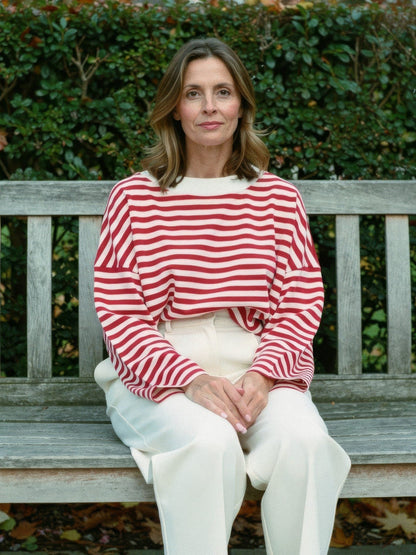 Woman wearing the cherry red breton stripe top with cream trousers on a garden bench
