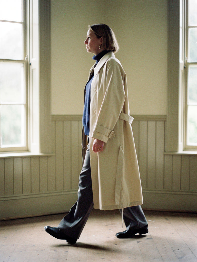 Brown coat in Beeswax, worn open and long in a bare panelled room