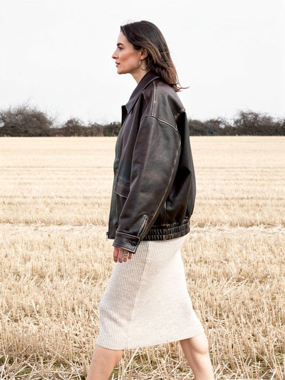 Womens brown jacket in distressed faux leather walking across a stubble field, side view, in Bison
