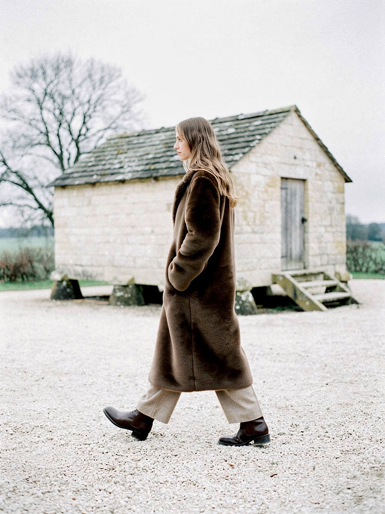 Brown faux fur coat seen in profile on a frosty Cotswold farmyard, hem falling to mid calf