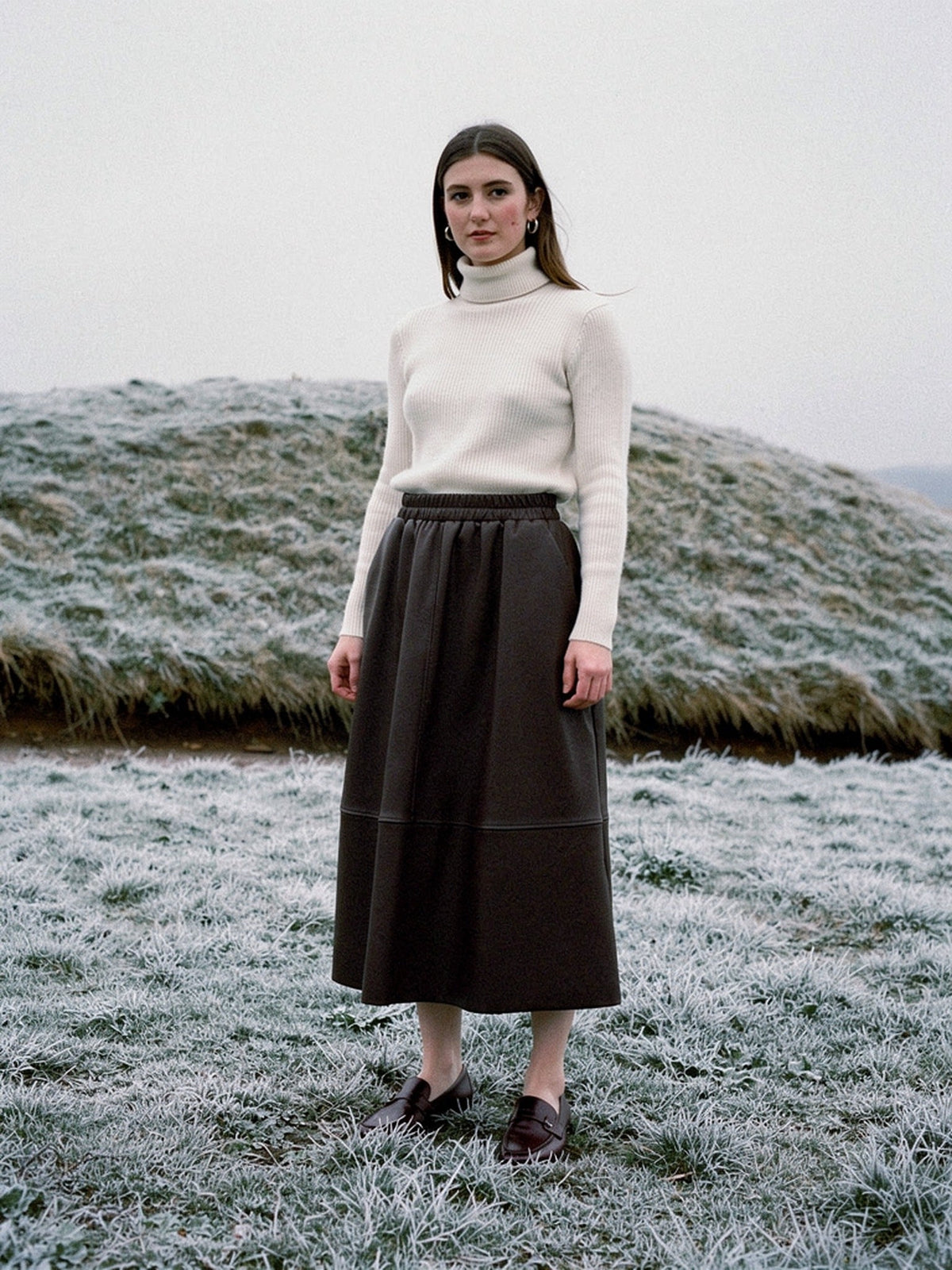 Brown faux leather skirt worn with a cream roll neck on a frosted English chalk down, the A line hem falling to the middle of the calf