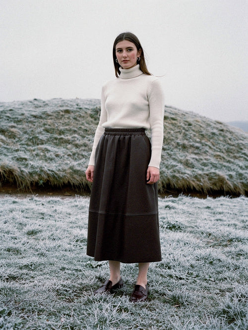 Brown faux leather skirt worn with a cream roll neck on a frosted English chalk down, the A line hem falling to the middle of the calf