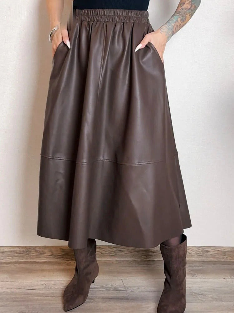 Maker photograph of the brown faux leather skirt worn, both hands in the slanted side pockets, showing the gathered waistband and the level seam low on the skirt