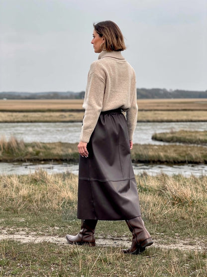 Brown faux leather skirt seen from behind on an estuary saltmarsh, showing how the A line hem swings as she walks