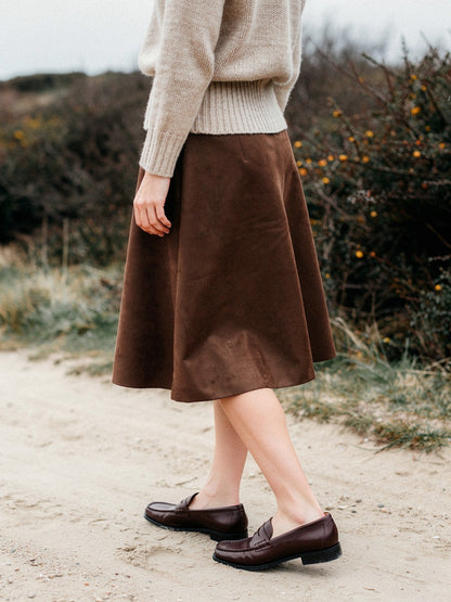 Brown faux suede skirt seen from behind on a sandy heath path, showing how the A line hem swings as she walks