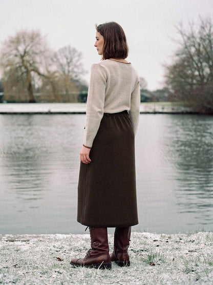 Brown skirt in a brushed A line midi cut, seen from behind beside a village pond, in Bog Oak