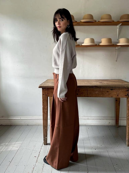 Brown trousers in Russet, high-waisted pleated wide leg, worn in a milliner's workroom