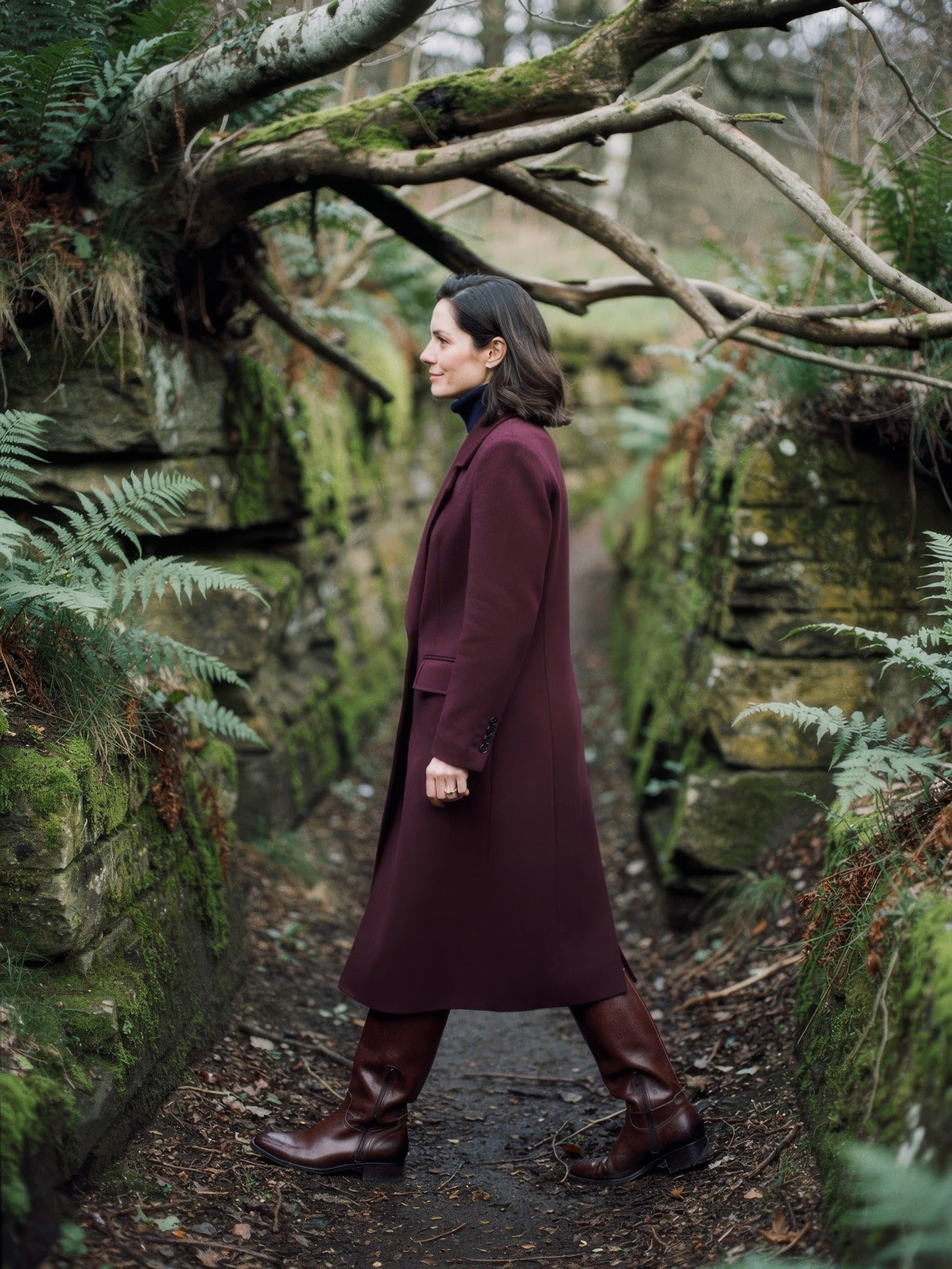 Burgundy coat seen from the side in a sunken country lane, showing the mid calf length, in Claret