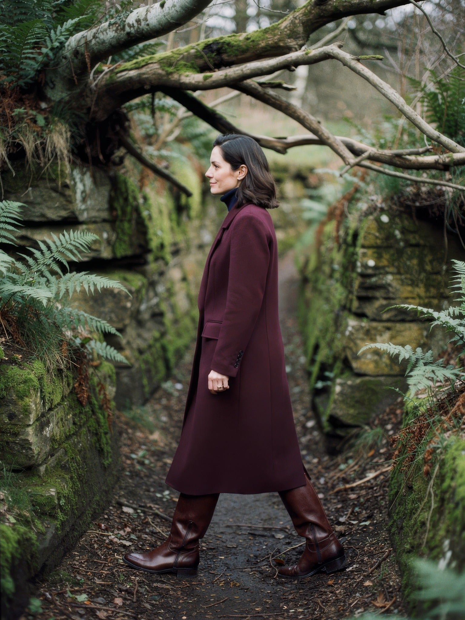 Burgundy coat seen from the side in a sunken country lane, showing the mid calf length, in Claret