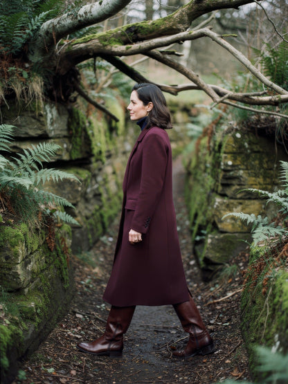 Burgundy coat seen from the side in a sunken country lane, showing the mid calf length, in Claret