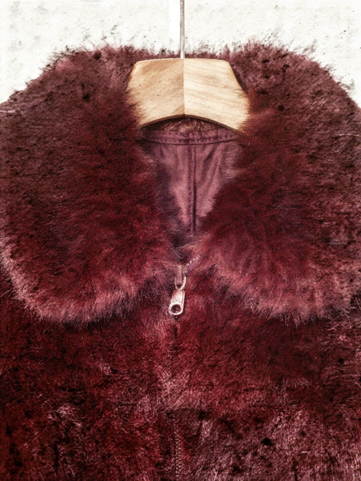 Wide turn down collar and centre zip pull of the burgundy faux fur jacket