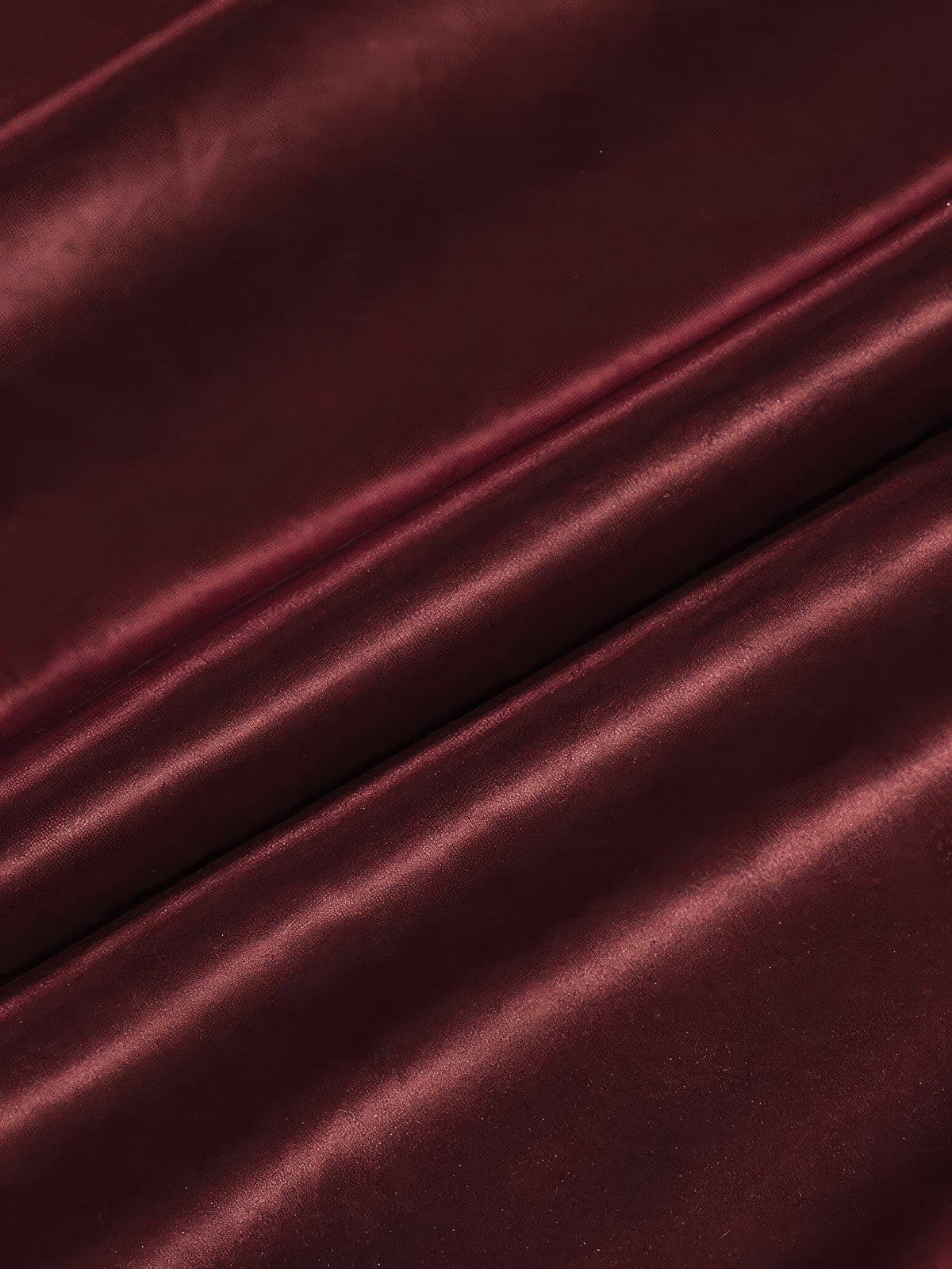 Close up of the wine red woven satin of the burgundy satin skirt, showing the broad soft bands of light across the folds