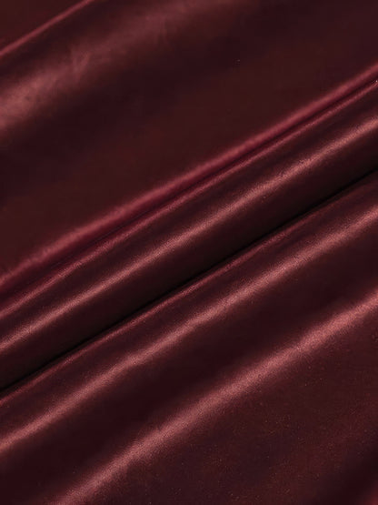 Close up of the wine red woven satin of the burgundy satin skirt, showing the broad soft bands of light across the folds