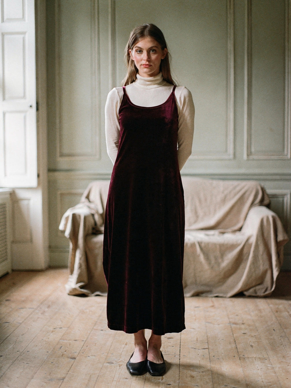 Burgundy velvet dress worn over a cream roll neck in a shuttered English drawing room