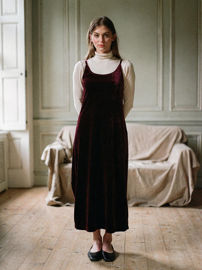 Burgundy velvet dress worn over a cream roll neck in a shuttered English drawing room