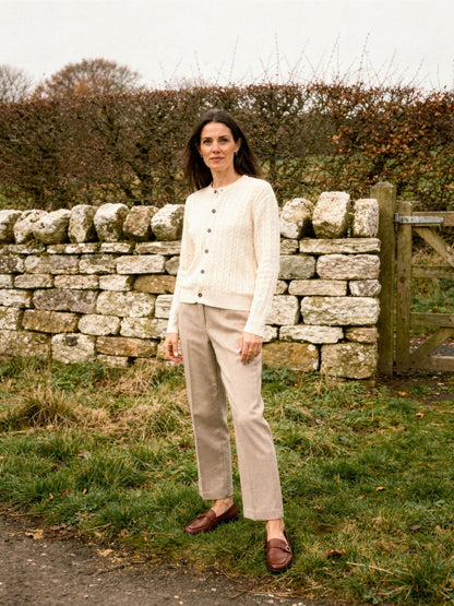 Womens cable knit cardigan in Creamware, buttoned, worn by a dry stone wall