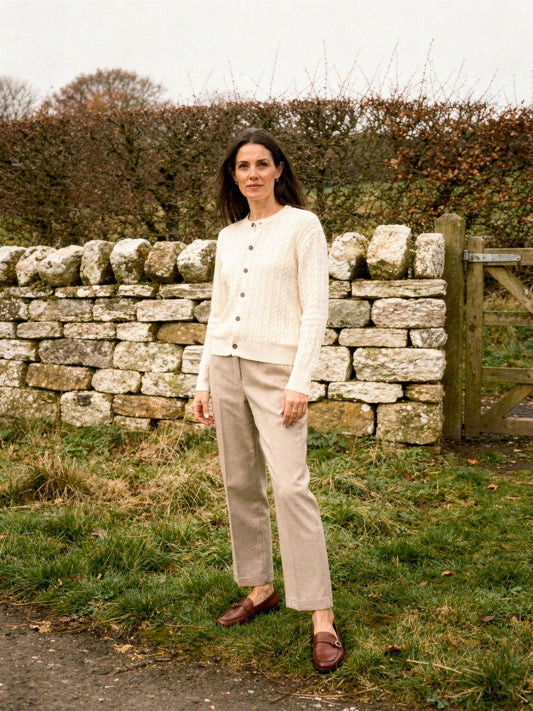 Womens cable knit cardigan in Creamware, buttoned, worn by a dry stone wall