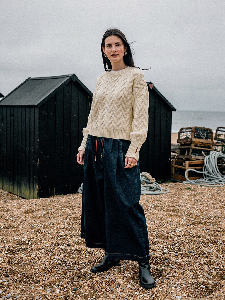 Woman wearing a cropped cable knit jumper in Shortbread cream on an English shingle beach