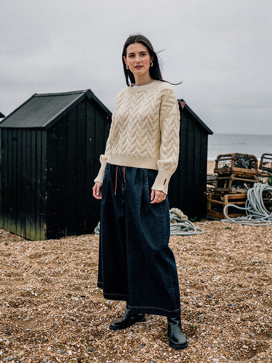 Woman wearing a cropped cable knit jumper in Shortbread cream on an English shingle beach